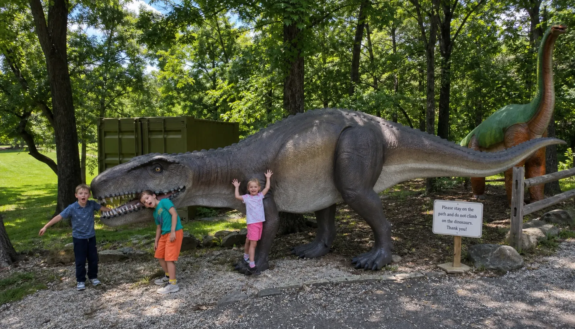 Kids posing with a life-size dinosaur on the wooded trail at Valley of the Dinosaurs