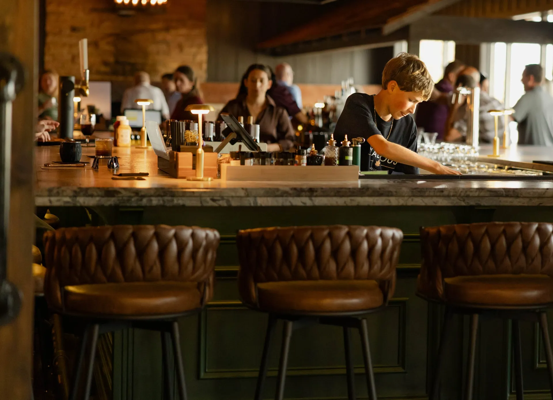 Bartenders at work behind the bar, with leather stools in the foreground