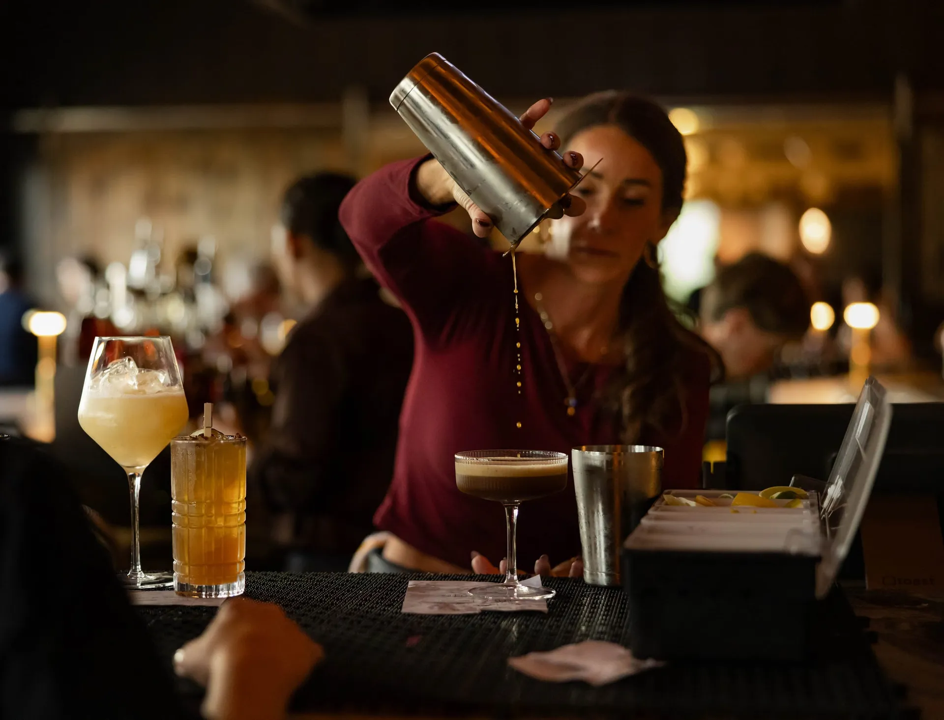 Bartender shaking a cocktail beside finished drinks on the bar