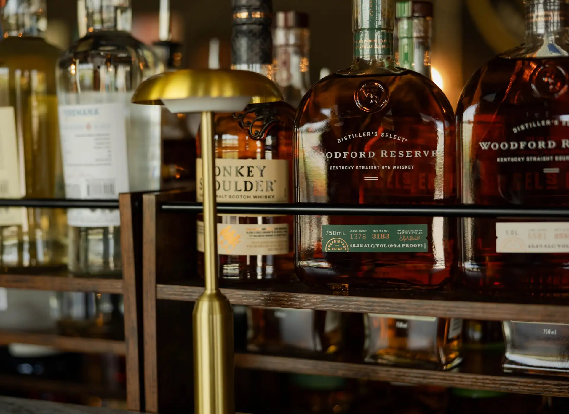 Bourbon bottles on the back bar beneath a brass lamp