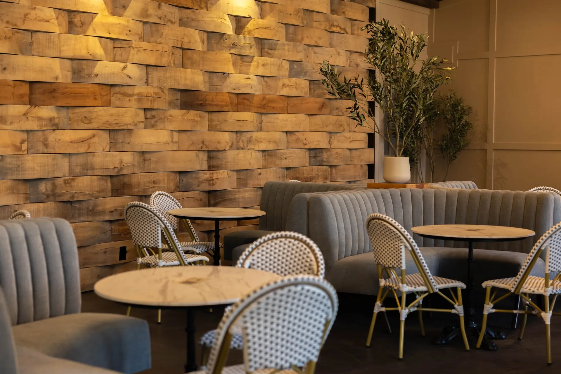 Tufted banquettes and marble bistro tables against the barrel-stave wall in The Press